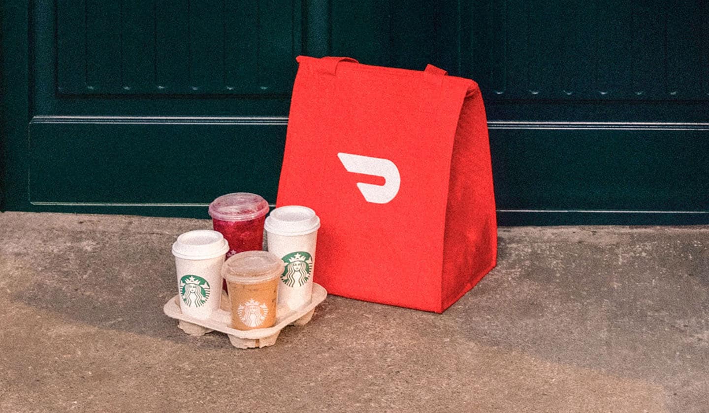 A red DoorDash bag sits next to a Starbucks drink carrier holding four beverages.