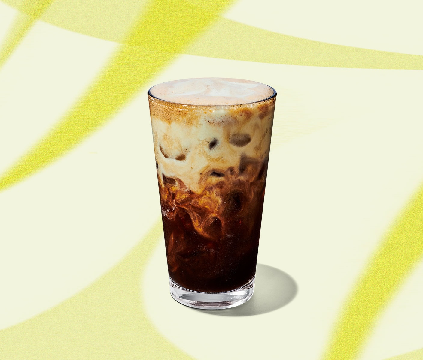 An iced coffee drink in a tall, clear glass with a creamy top half.
