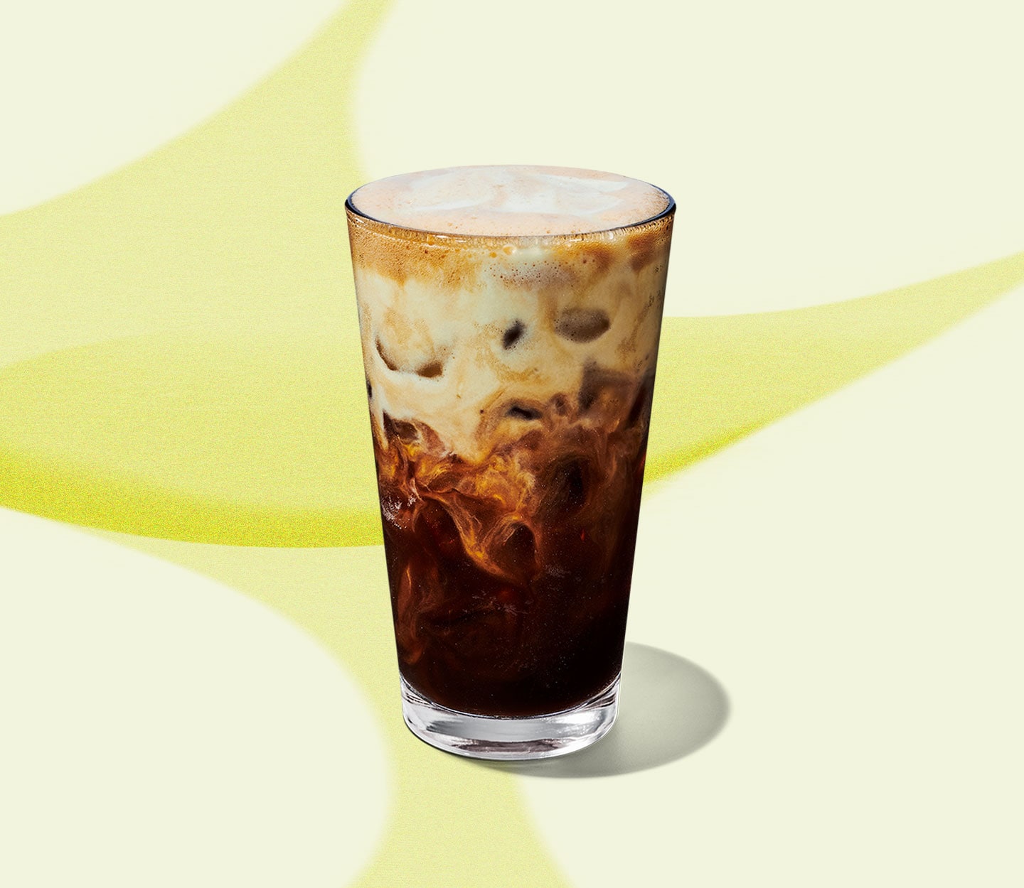 An iced coffee drink in a tall, clear glass with a creamy top half.