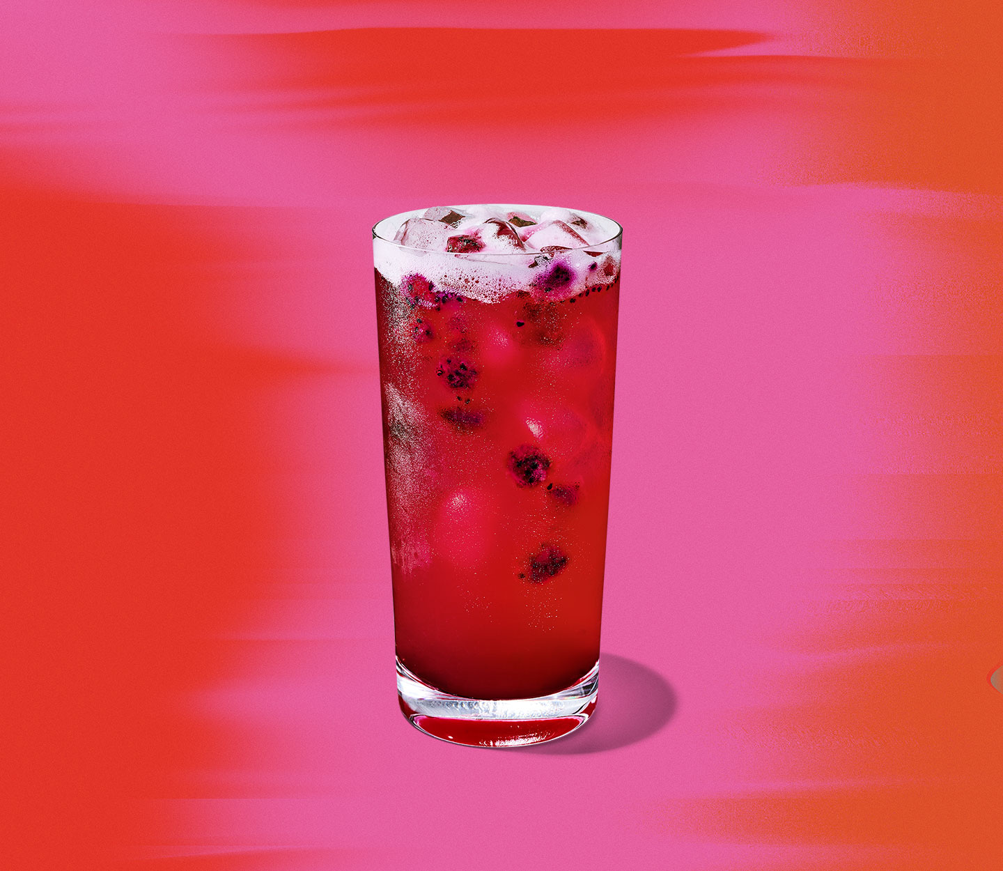 A red iced drink with pieces of dragonfruit floating in a tall glass.