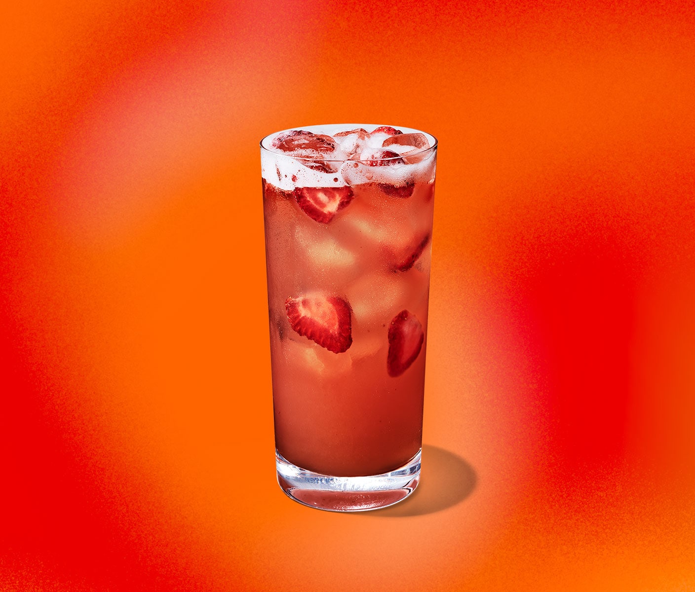 A red iced drink with pieces of strawberries floating in a tall glass.