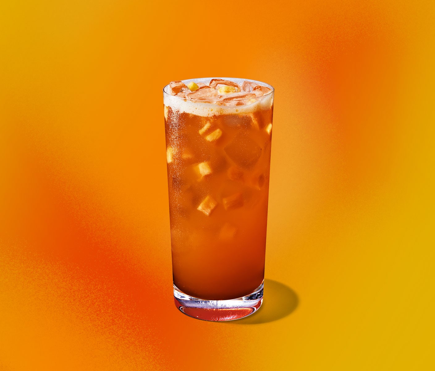 An orange iced drink with pieces of pineapple floating in a tall glass.