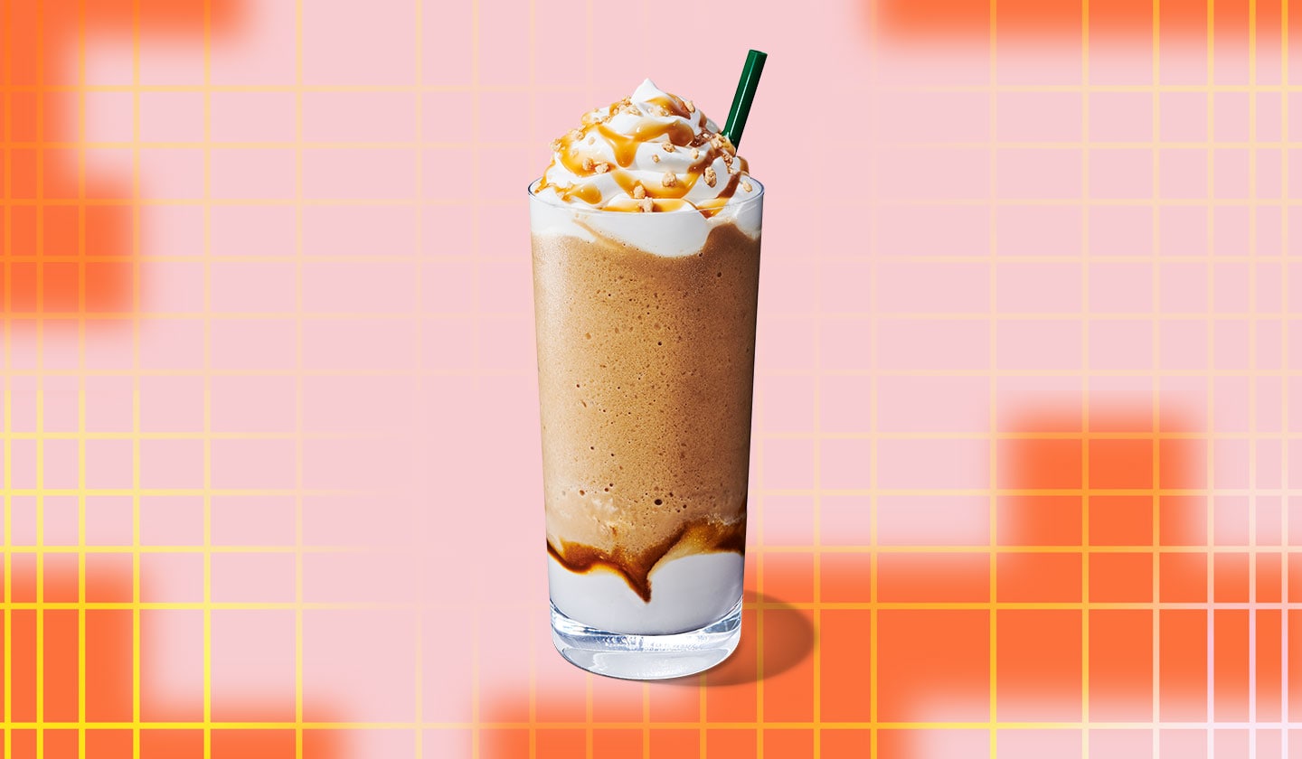 A blended coffee drink in a tall glass with whipped cream on top and a straw.