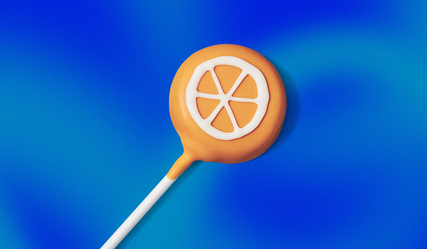 A cake pop with a white design in the shape of an orange slice.