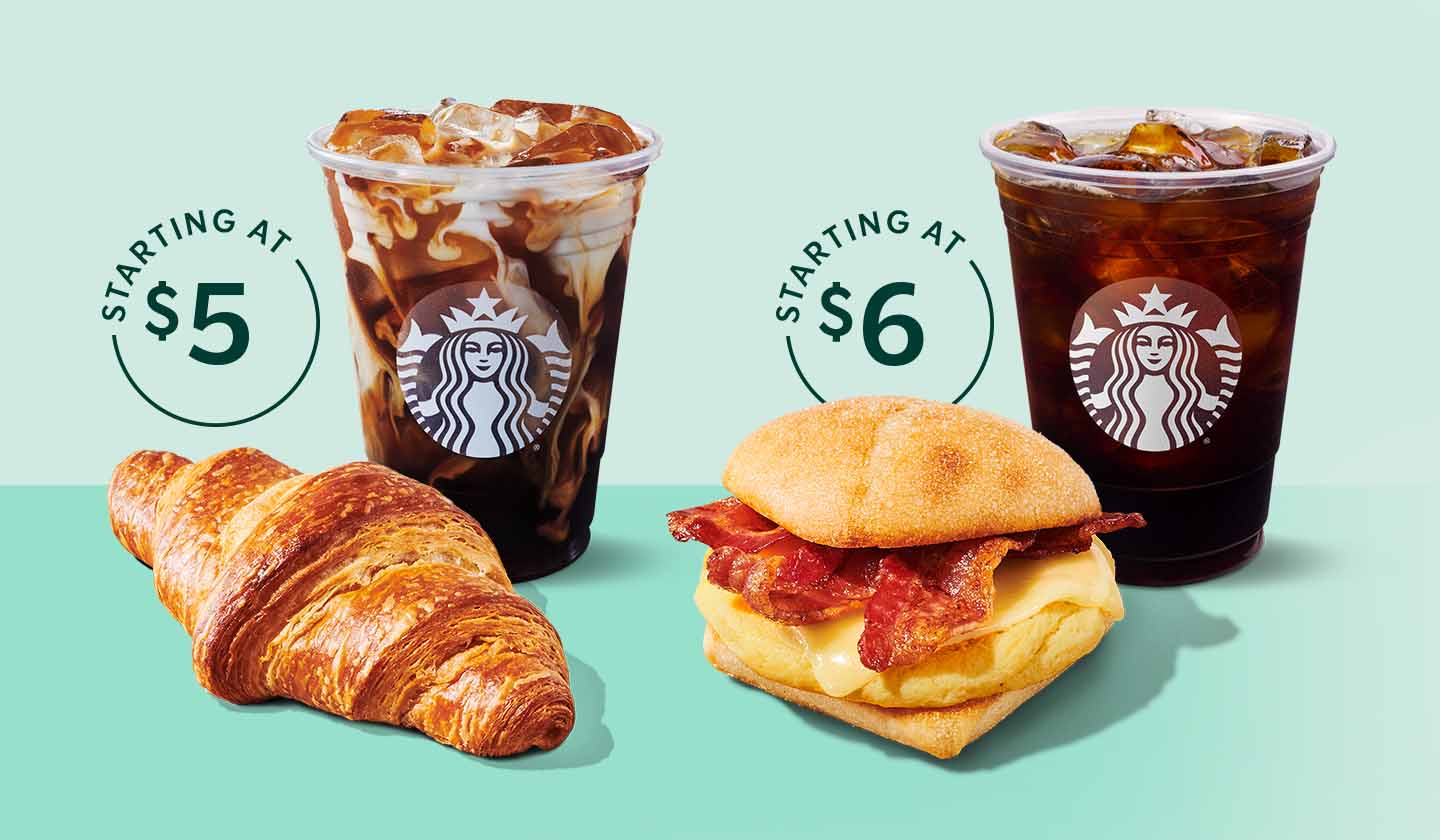 Two cups of Starbucks iced coffee sit behind a croissant and a breakfast sandwich.