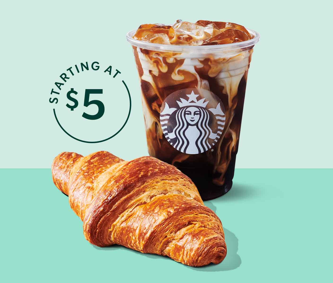 A cup of Starbucks iced coffee with milk sits behind a croissant.