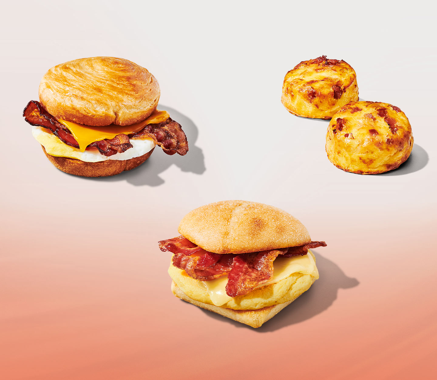 Two hot breakfast sandwiches revealing bacon and egg between a roll, and a pair of round egg forms revealing chopped bacon.