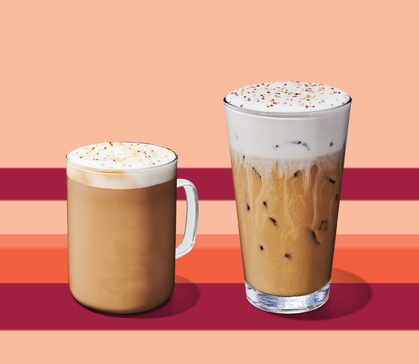 A creamy hot coffee drink with a frothy top in a glass mug next to an iced creamy coffee drink with a foamy top in a tall glass.