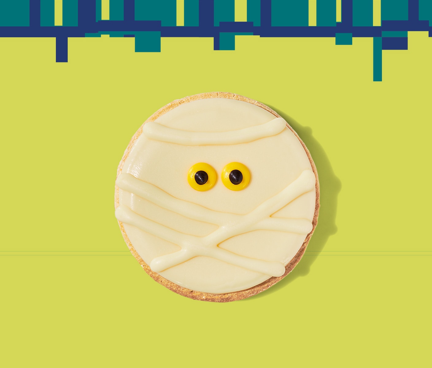 A round cookie with white icing in a mummy face including small eyes.