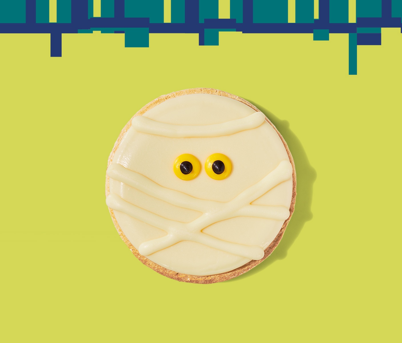 A round cookie with white icing in a mummy face including small eyes.