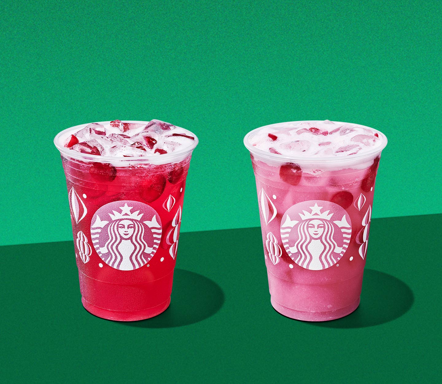 Two cold drinks in festive patterned cups: one is red and the other is pink, both with pieces of floating cranberries.