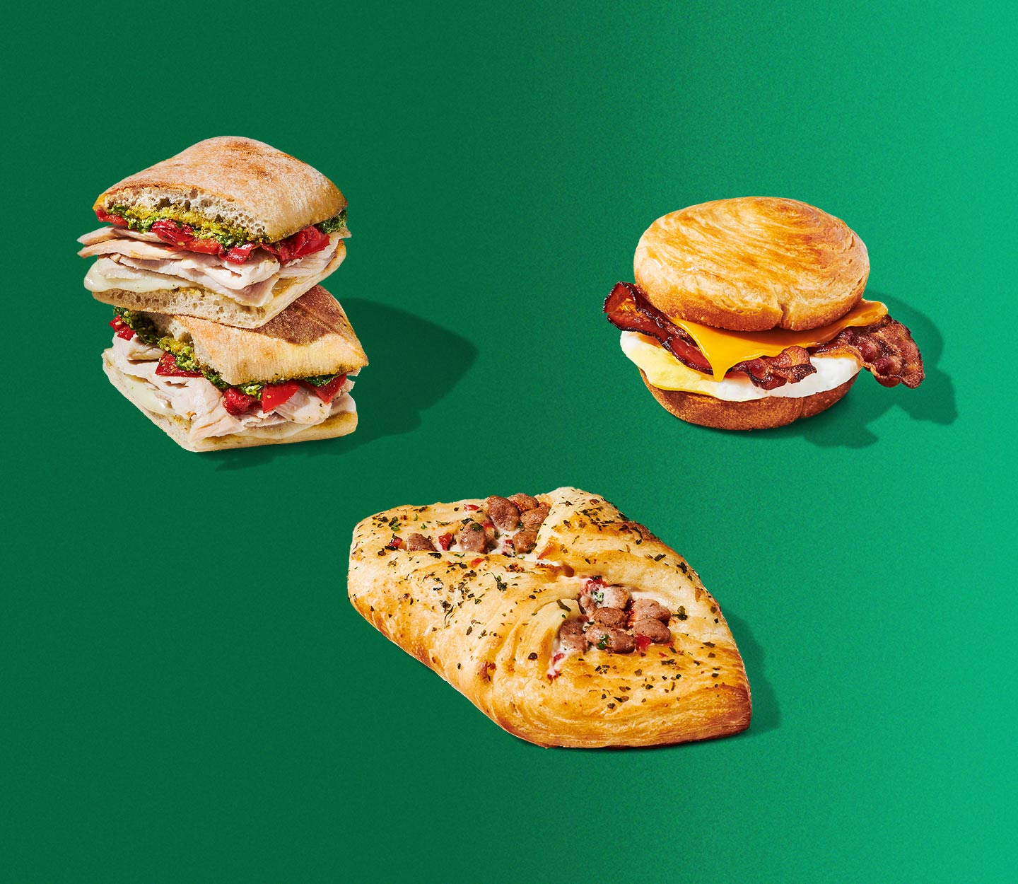 A sandwich cut in half and stacked, a flaky, golden-brown danish with a turkey filling, and a round sandwich with bacon and cheese.