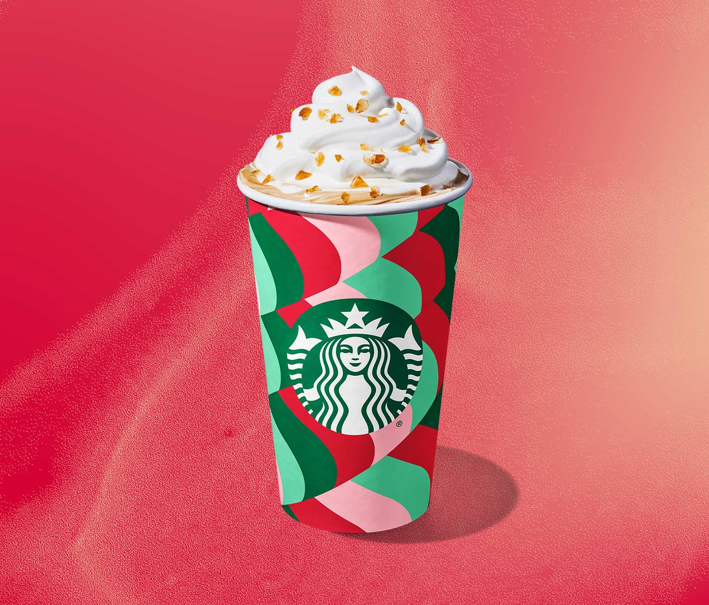 A hot coffee drink in a festive red and green patterned cup with a whipped cream topping and crunchy caramel brulée pieces.