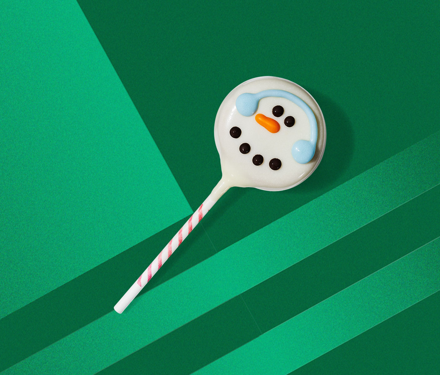 A cake pop with a snowman face design and blue earmuffs drawn on.