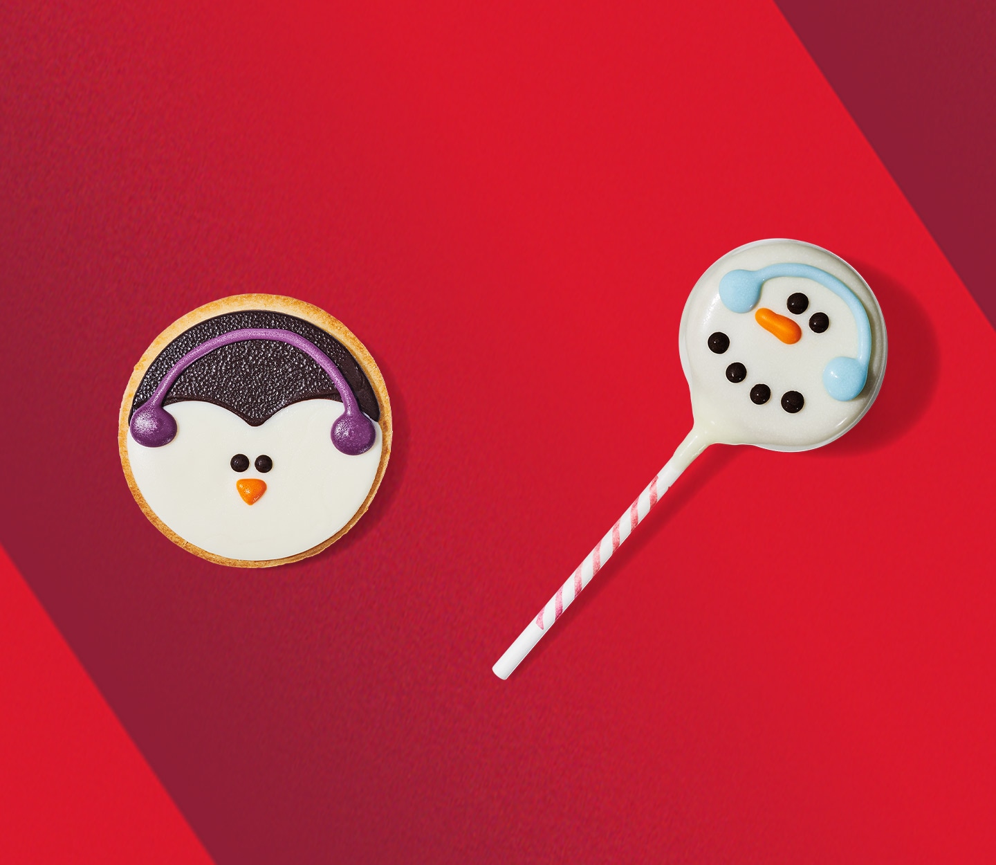 A round sugar cookie with a penguin face wearing earmuffs design and a cake pop with a snowman wearing earmuffs design.