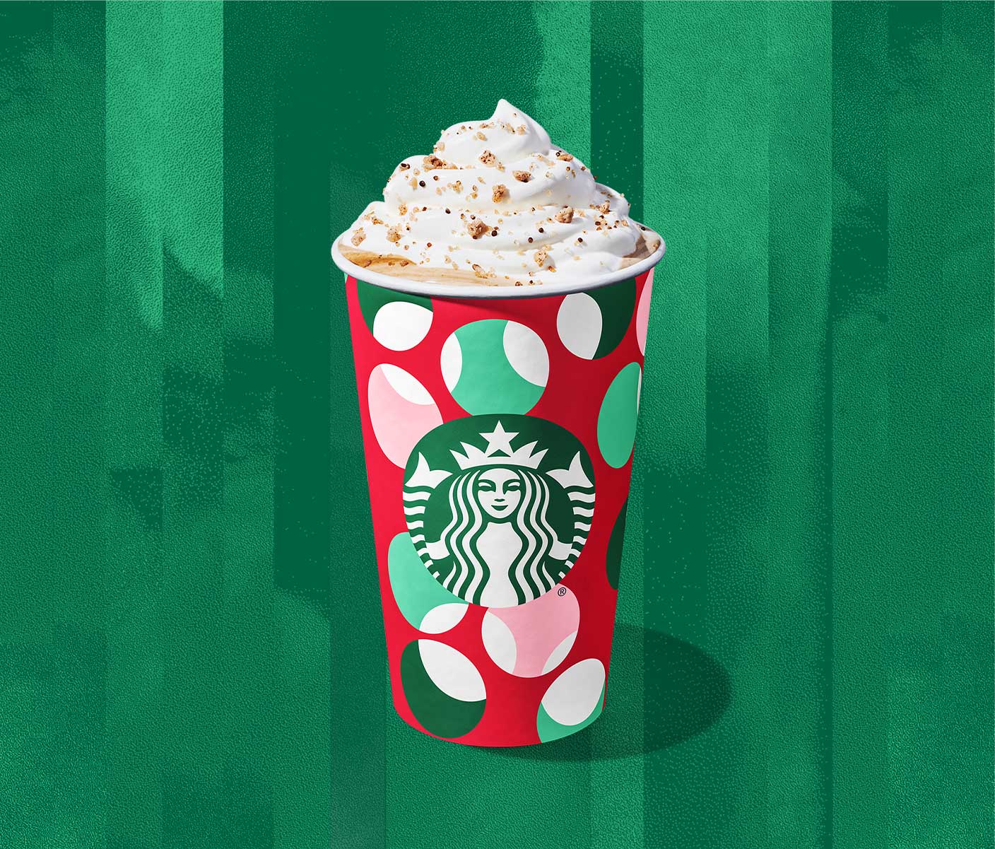 A hot coffee drink in a festive red and green patterned cup with a whipped cream topping and praline crumbs.