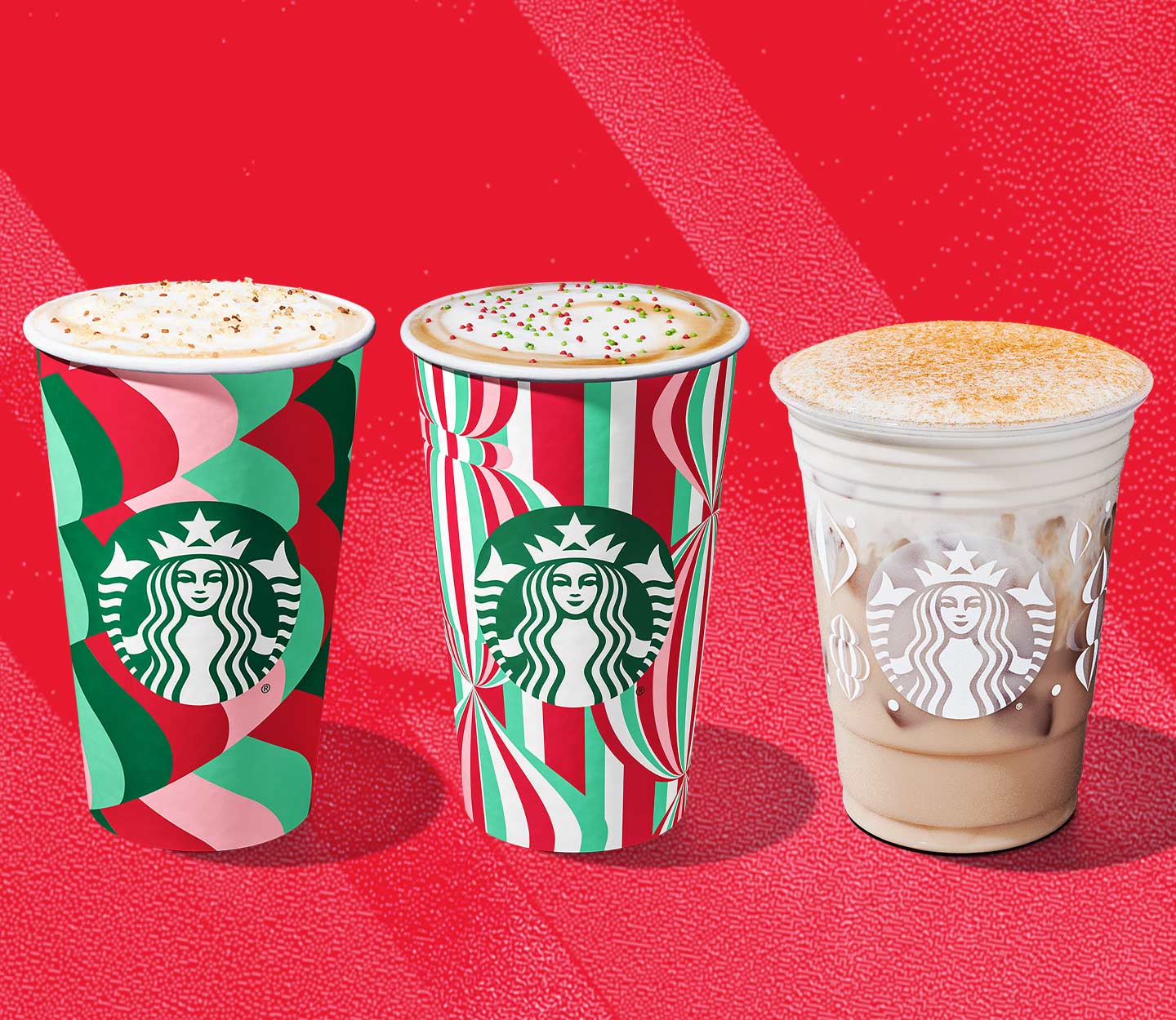 A trio of drinks in festive red, green and white patterned cups: two hot drinks with a frothy top, one iced with a thick layer of creamy foam.