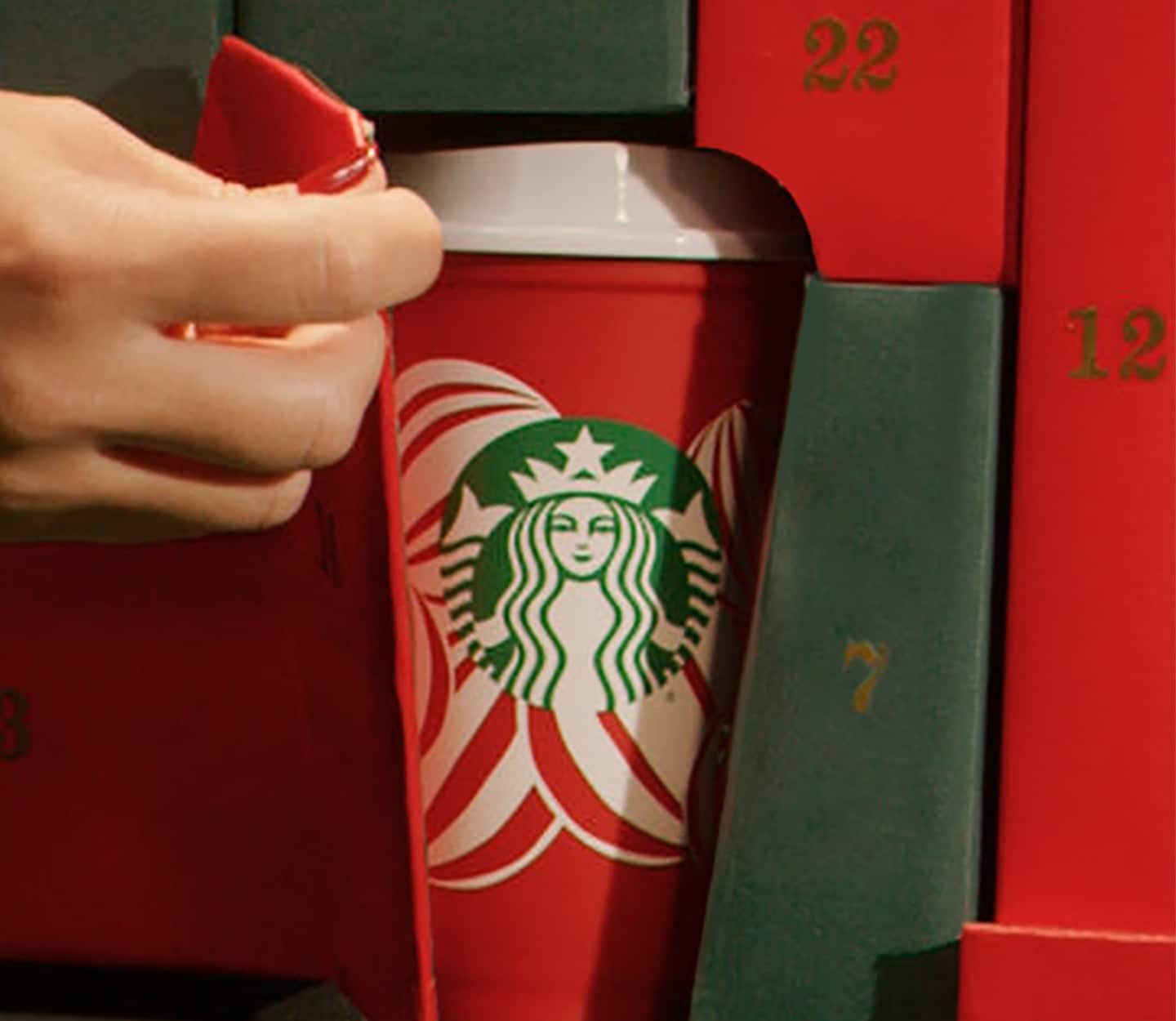 A reusable red Starbucks cup with a red and white ornament design peeks out of a red and green advent calendar.