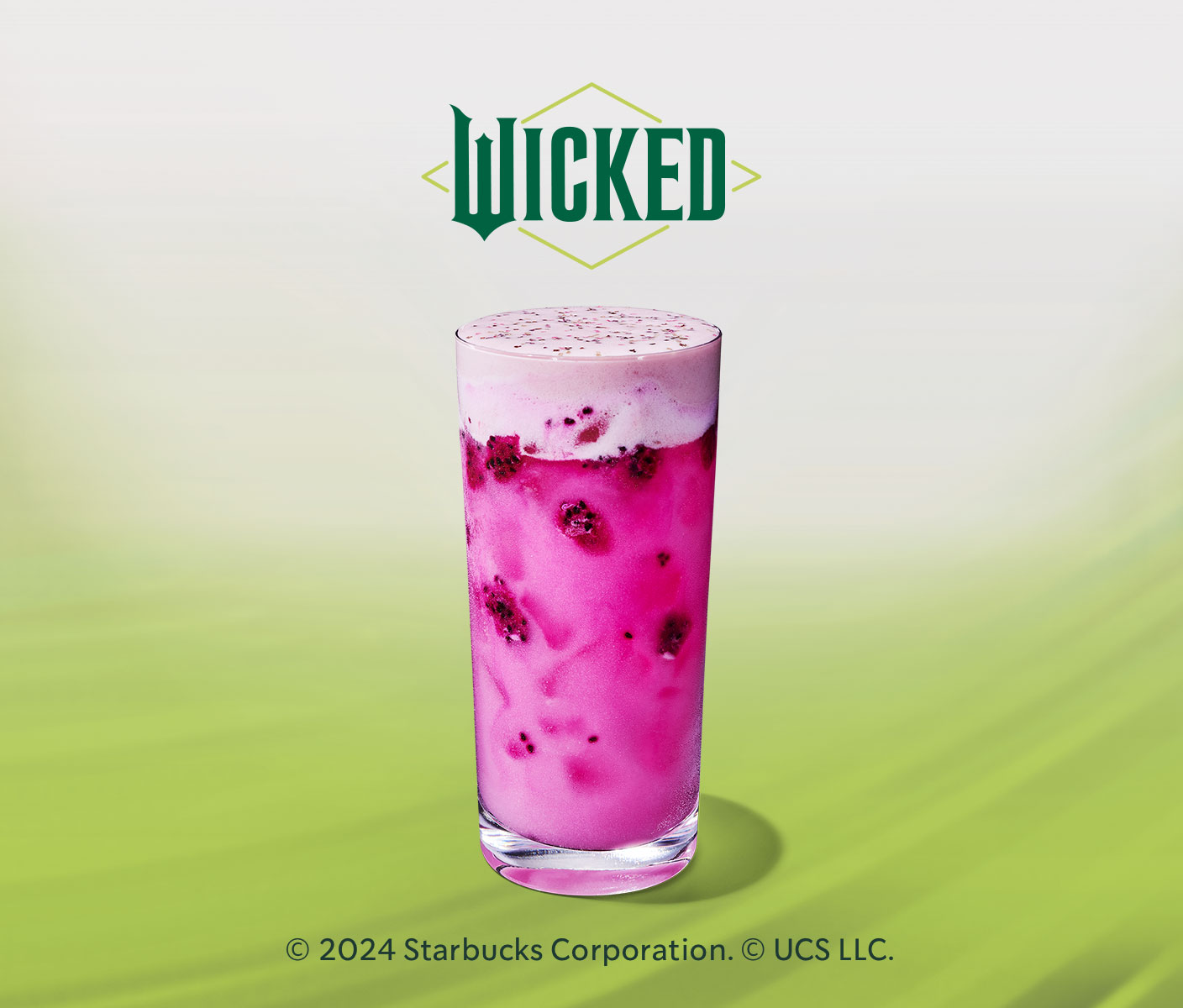 A bright pink iced drink with pieces of real dragonfruit in it, topped with a creamy layer of light pink foam and pink and green sprinkles.