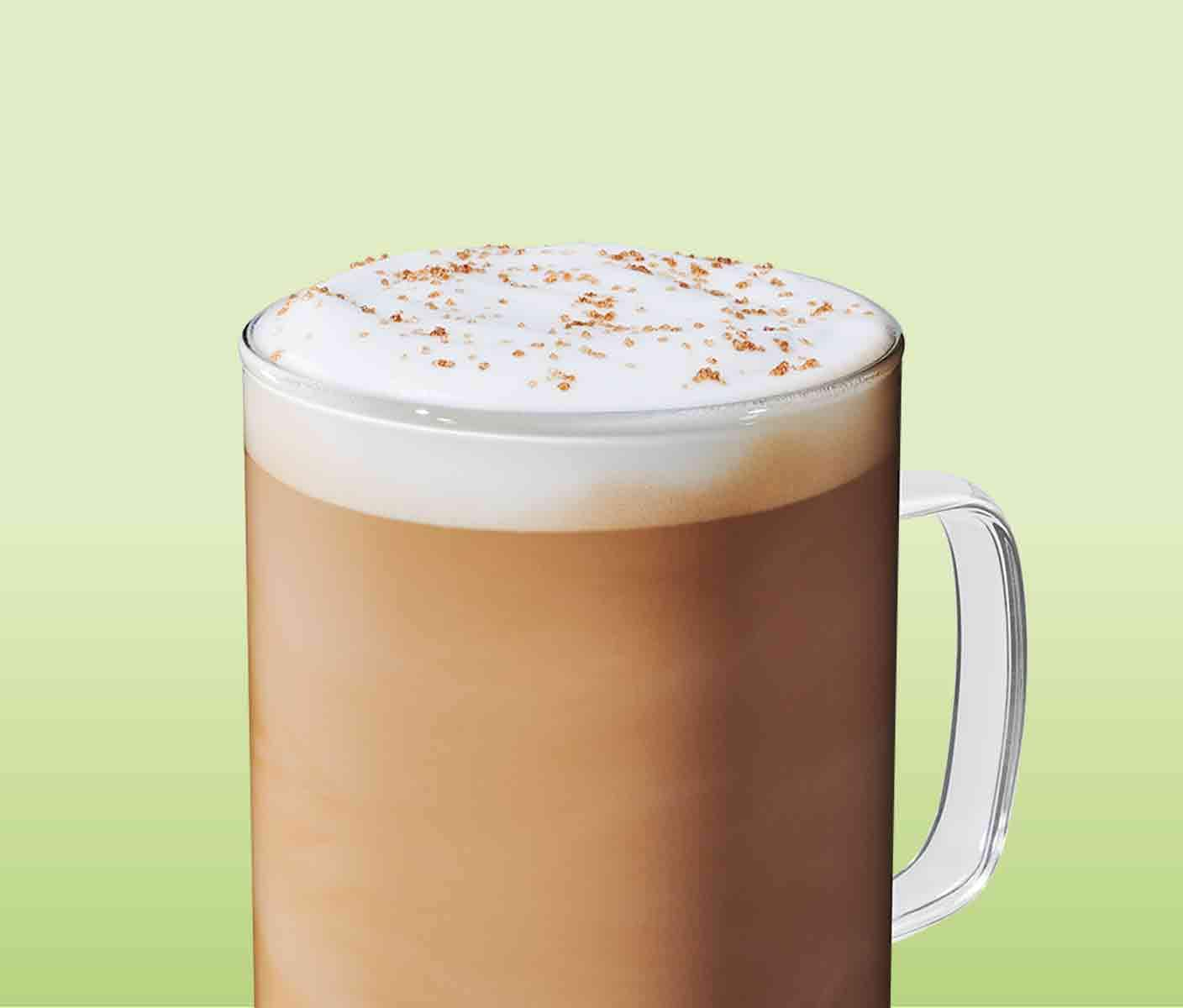 A creamy coffee drink with a frothy top in a glass mug with light brown sprinkles.