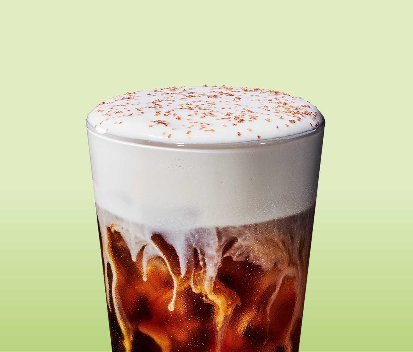 A cold coffee topped with foam and sprinkles in a tall glass with light brown sprinkles.