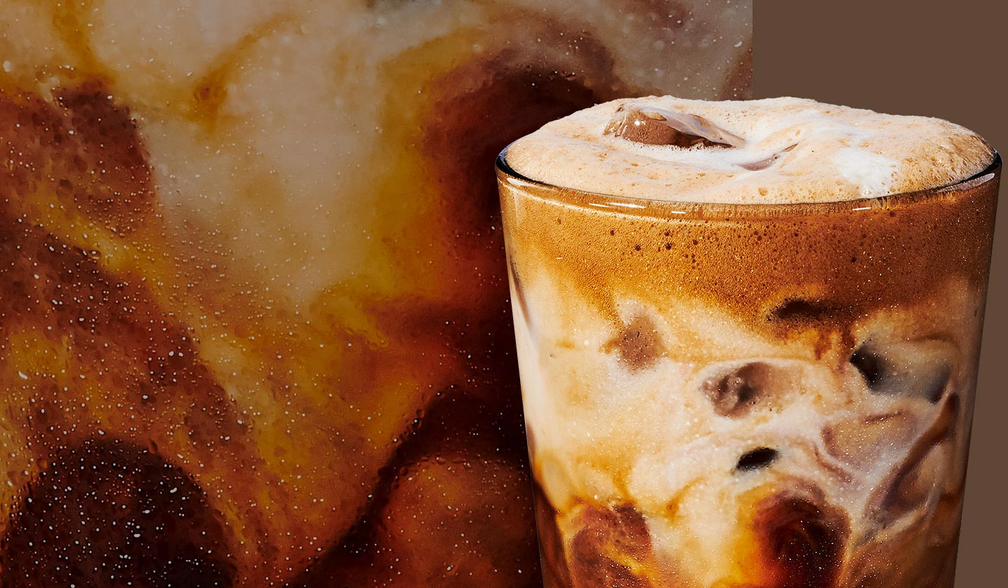 A tall glass of black coffee with cream against a close up shot of of coffee and cream.