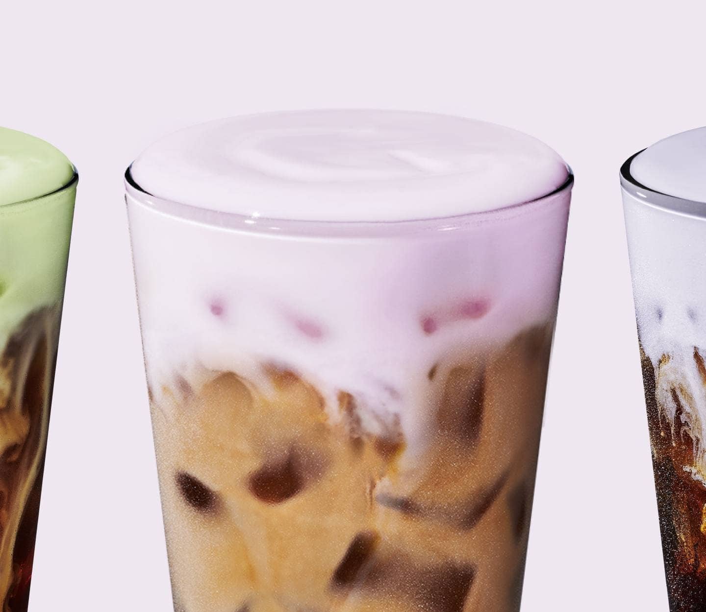 A layer of Cherry Cream Cold Foam on top of a cold coffee drink in a glass. Partially visible to the left and right are two other cold coffees topped with Matcha Cream Cold Foam and Lavender Cream Cold Foam, respectively.