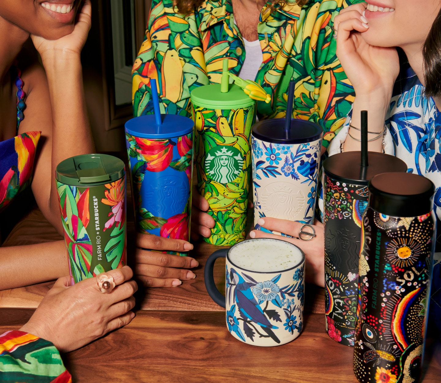 Photograph of a group of people gathered around a table with an assortment of Starbucks mugs and tumblers with vibrant, tropical-inspired patterns.