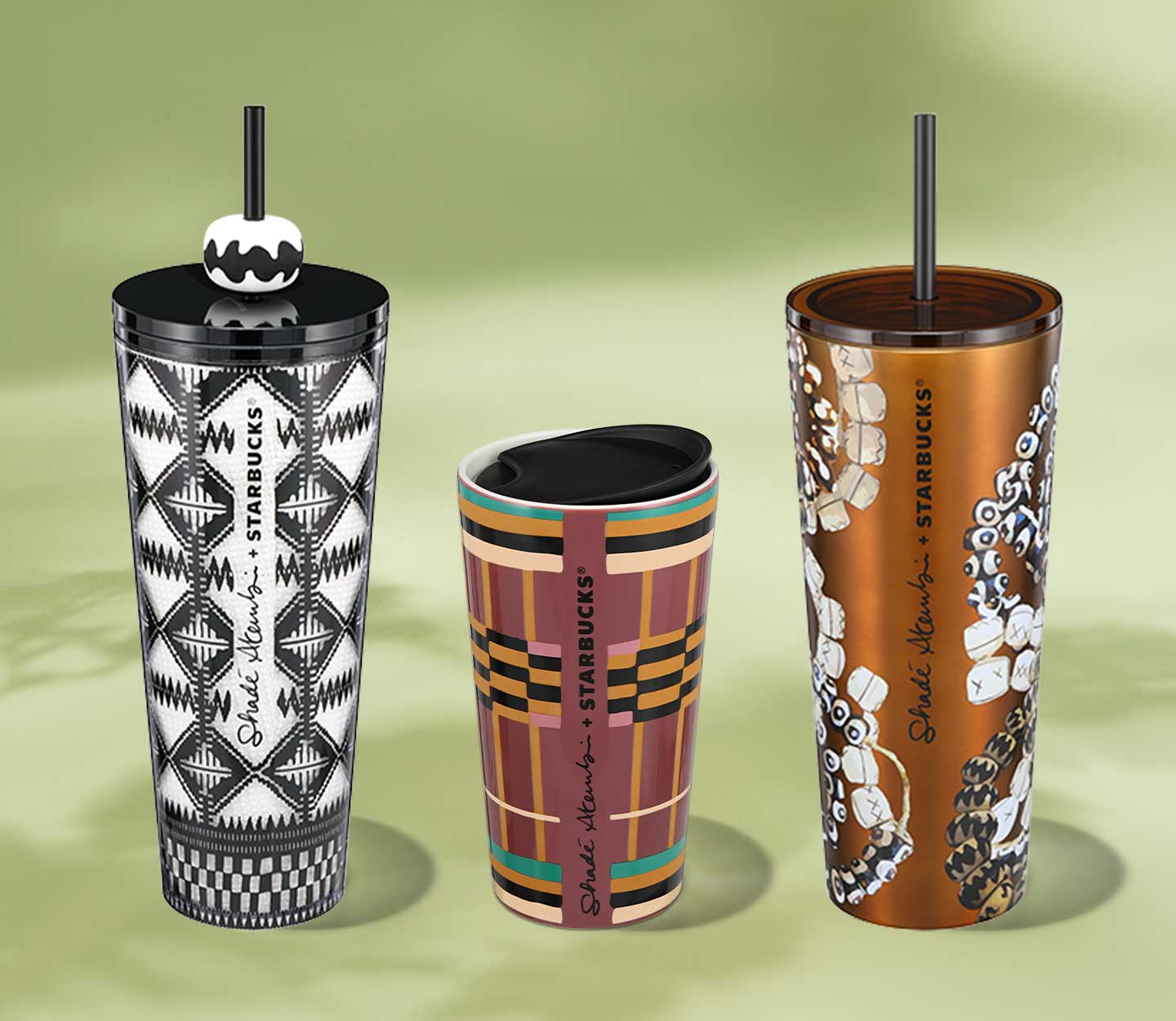 A ceramic tumbler with earth-toned geometric design and black lid is next to two cold cups with black lids and straws, one has a black and white geometric design, the other with a beaded jewelry design on bronze metallic background.