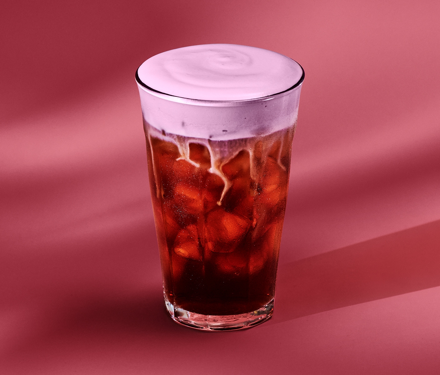 The new Raspberry Cream Cold Brew in a glass cup on a reddish-pink background.