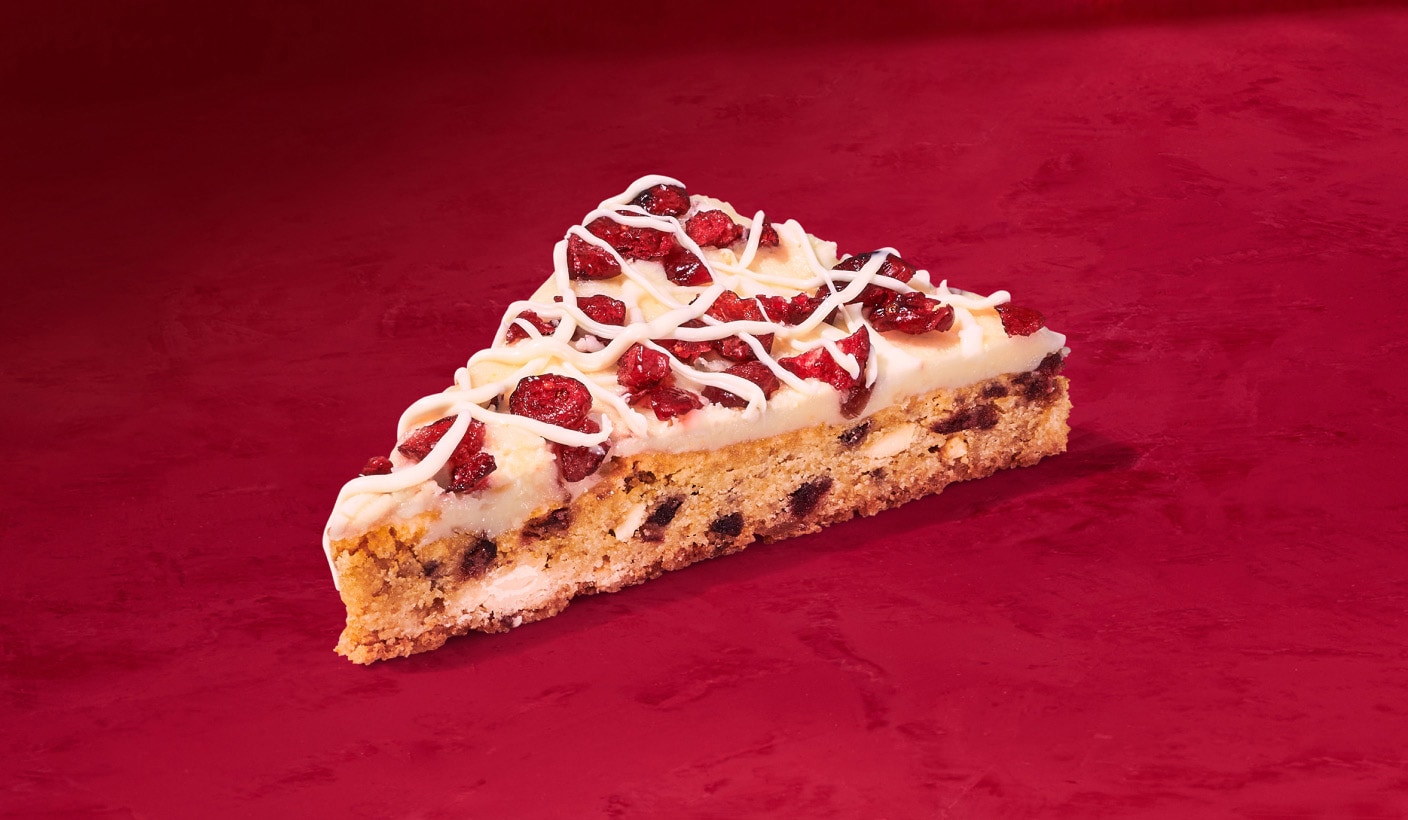A blondie loaded with cranberry pieces and a delicious drizzle of white chocolate on a red background.