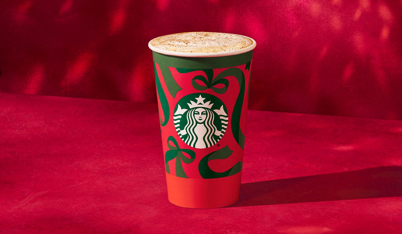 An iced espresso drink in a holiday cup topped with red and green holiday sprinkles on a red background.