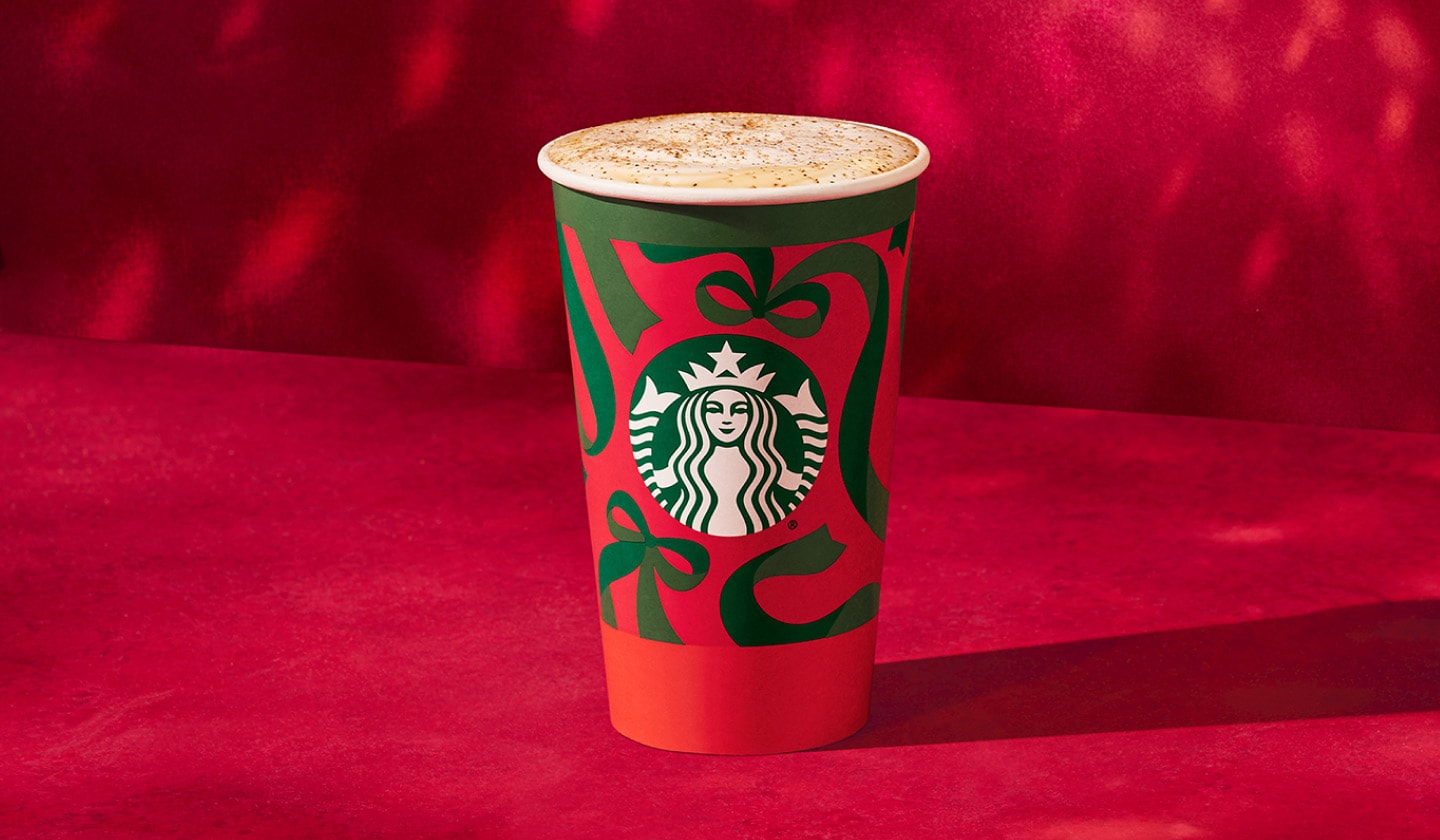 An iced espresso drink in a holiday cup topped with red and green holiday sprinkles on a red background.