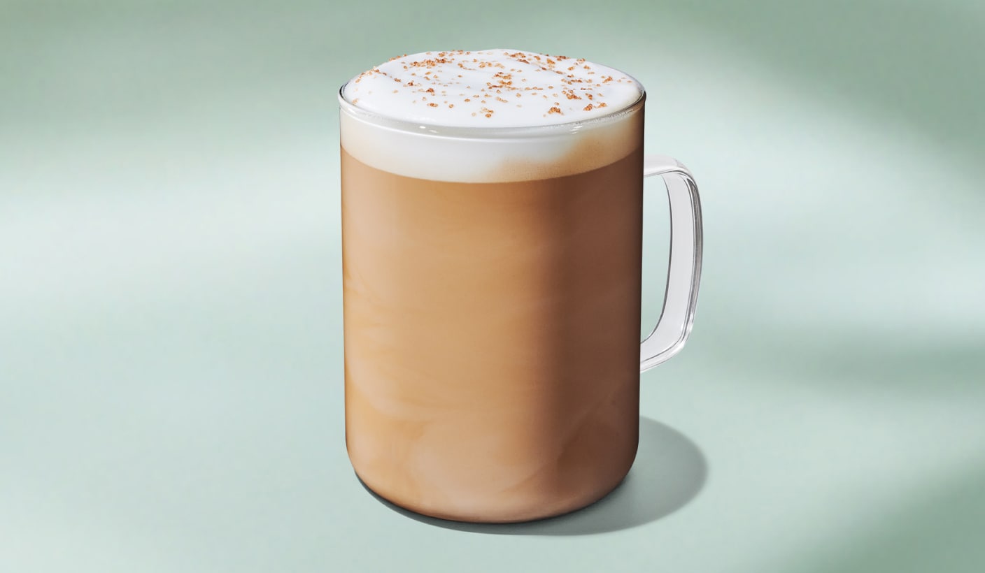 A perfectly steamed latte with a layer of milk foam, topped with crunchy brown butter sprinkles on a minty green background.