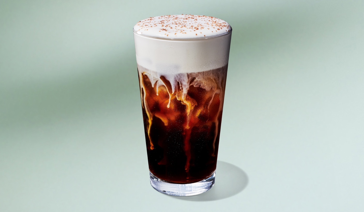 A refreshing cold brew with a thick, fluffy layer of cold foam and salted brown-buttery sprinkles slowly marbling it’s way through the drink on a minty green background.