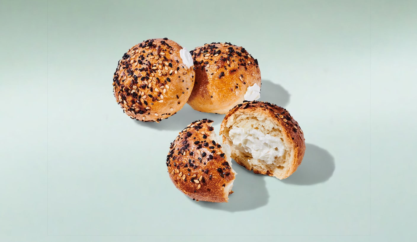 Three 2-bite sized bagel rounds, one of them broken apart to showcase the cream cheese inside, on a minty green background.