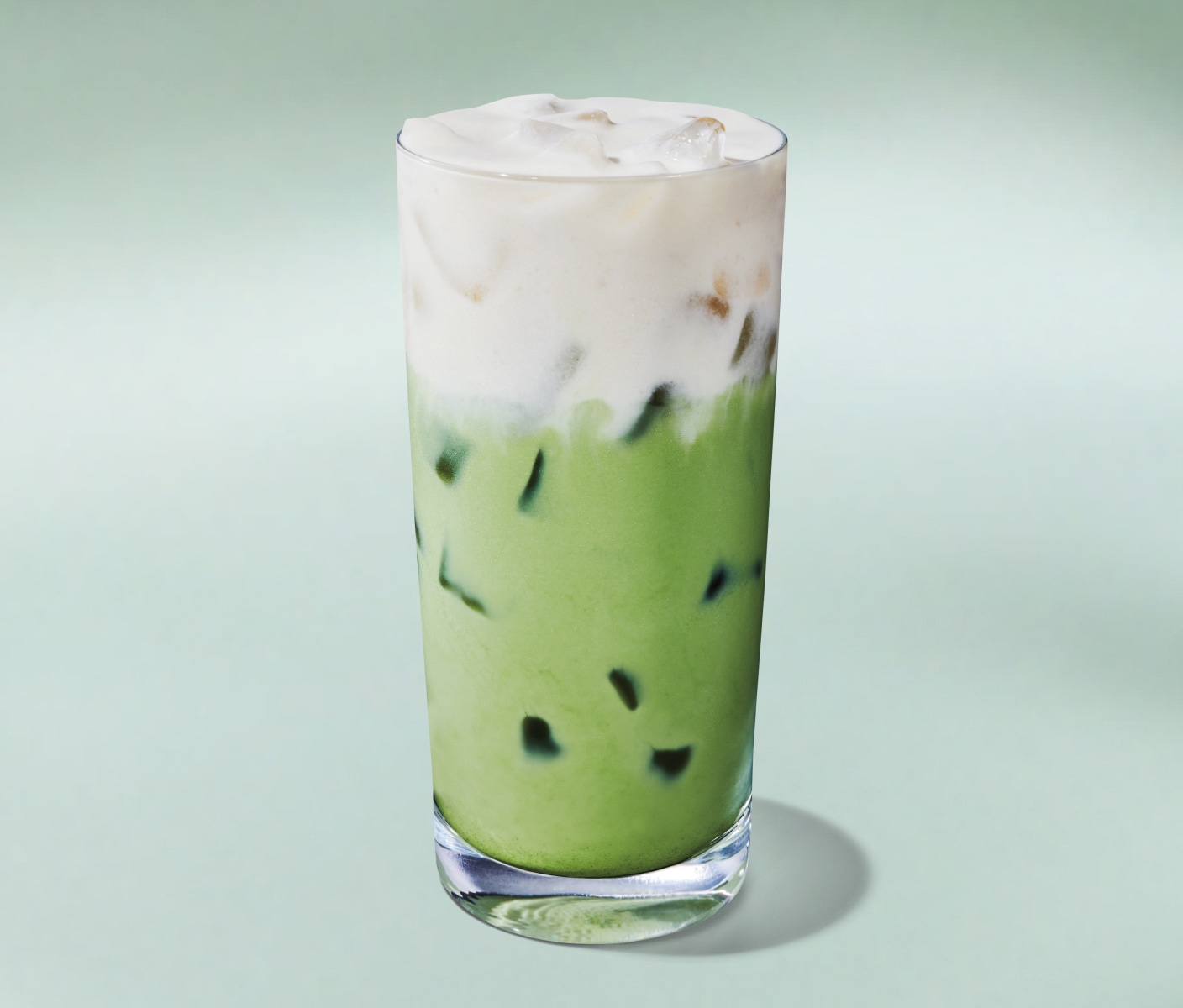 A vibrant green Iced Matcha Latte topped with fluffy cold foam on a minty green background.