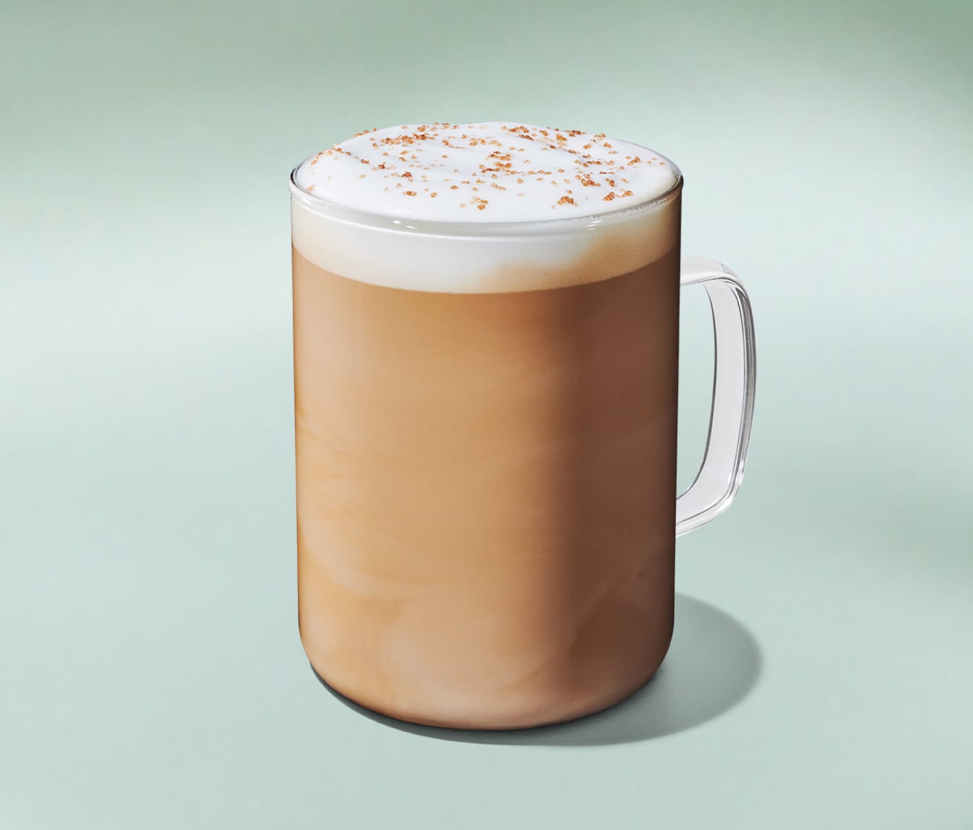 A perfectly steamed latte with a layer of milk foam, topped with crunchy brown butter sprinkles on a minty green background.