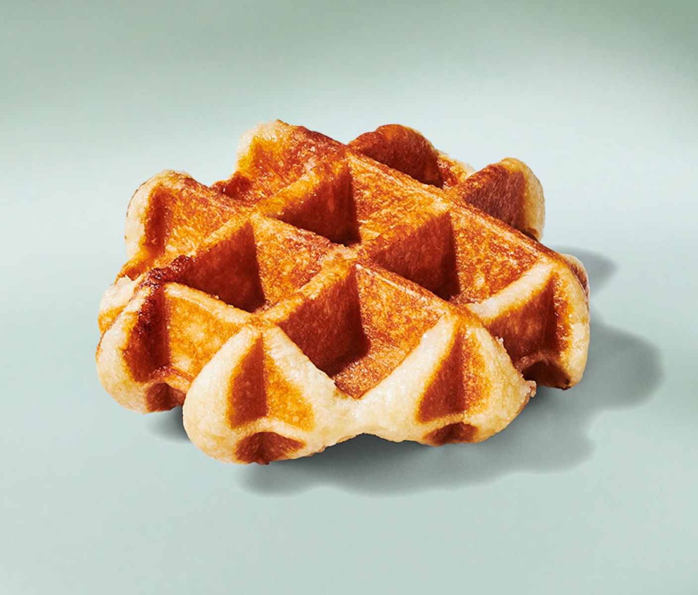 A beautiful, golden-brown waffle with sugar crystals on a minty green background.