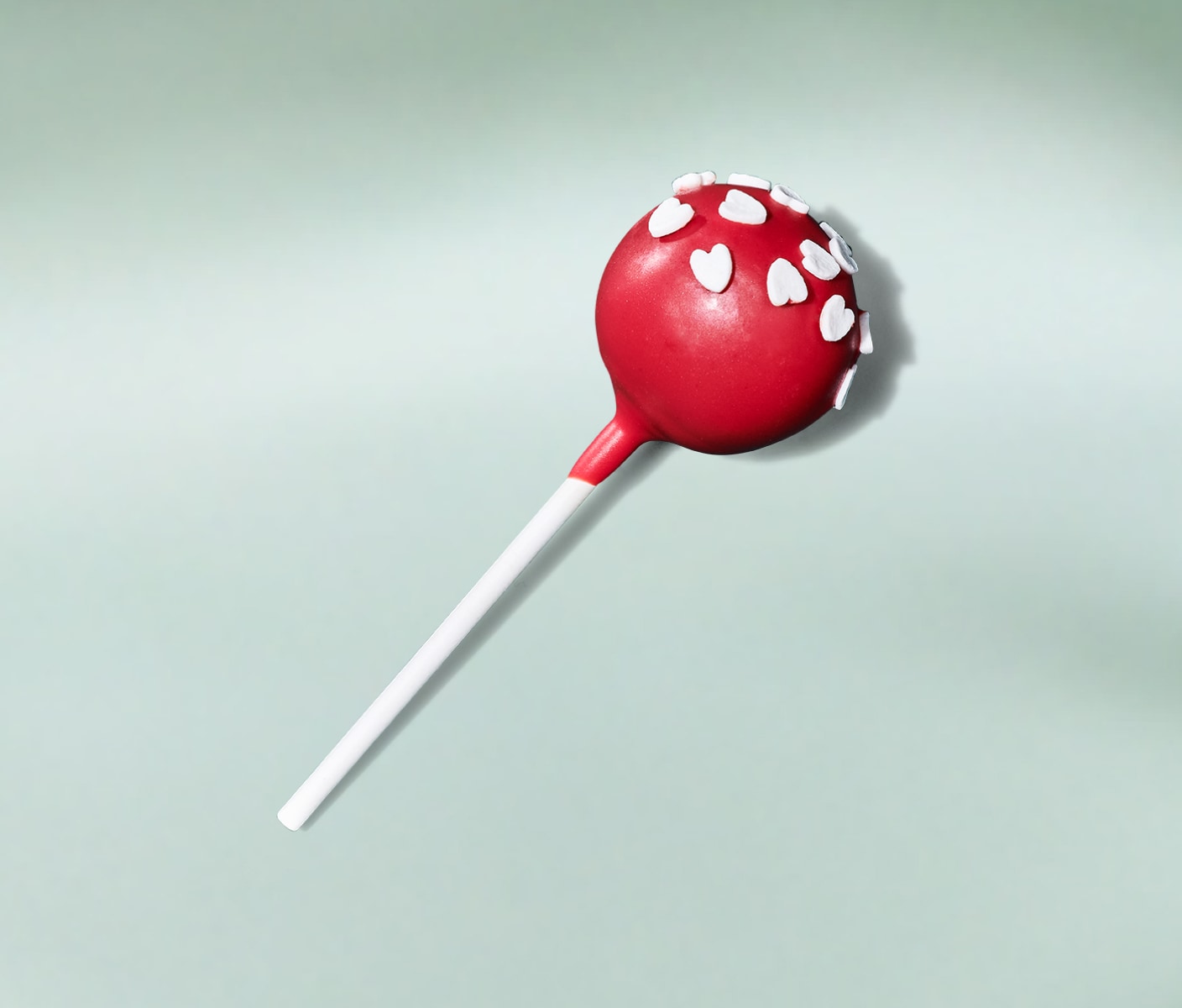 A festive, bright red cake pop with heart-shaped sprinkles on a minty green background. 
