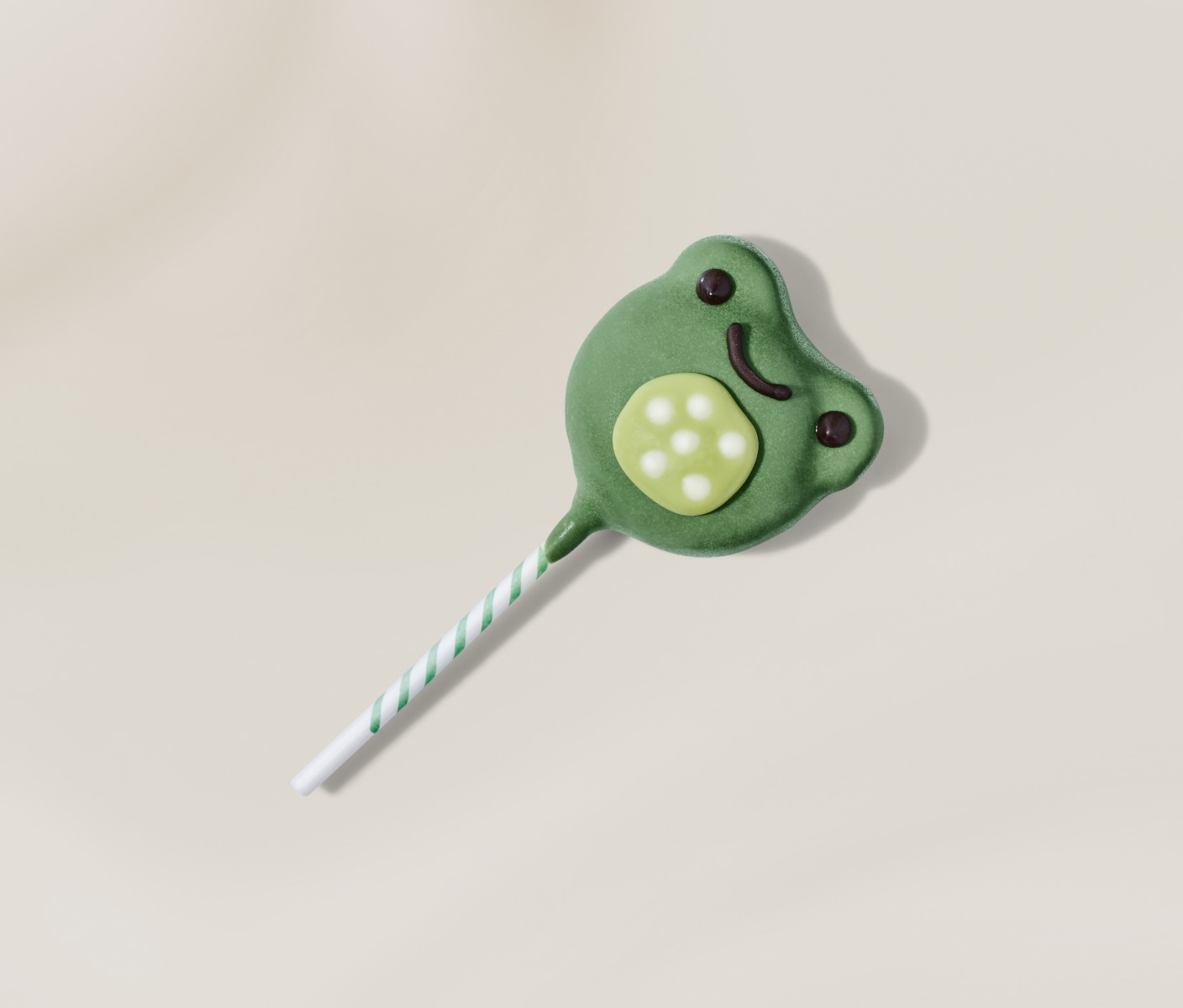 Frog-shaped cake pop with green chocolaty coating and playful details, displayed on a neutral background.