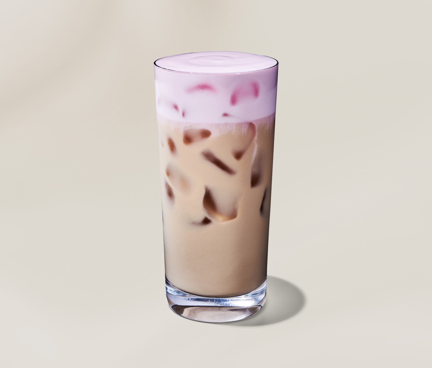 An iced chai latte in a clear glass topped with light pink cherry-flavoured cold foam on a neutral background.