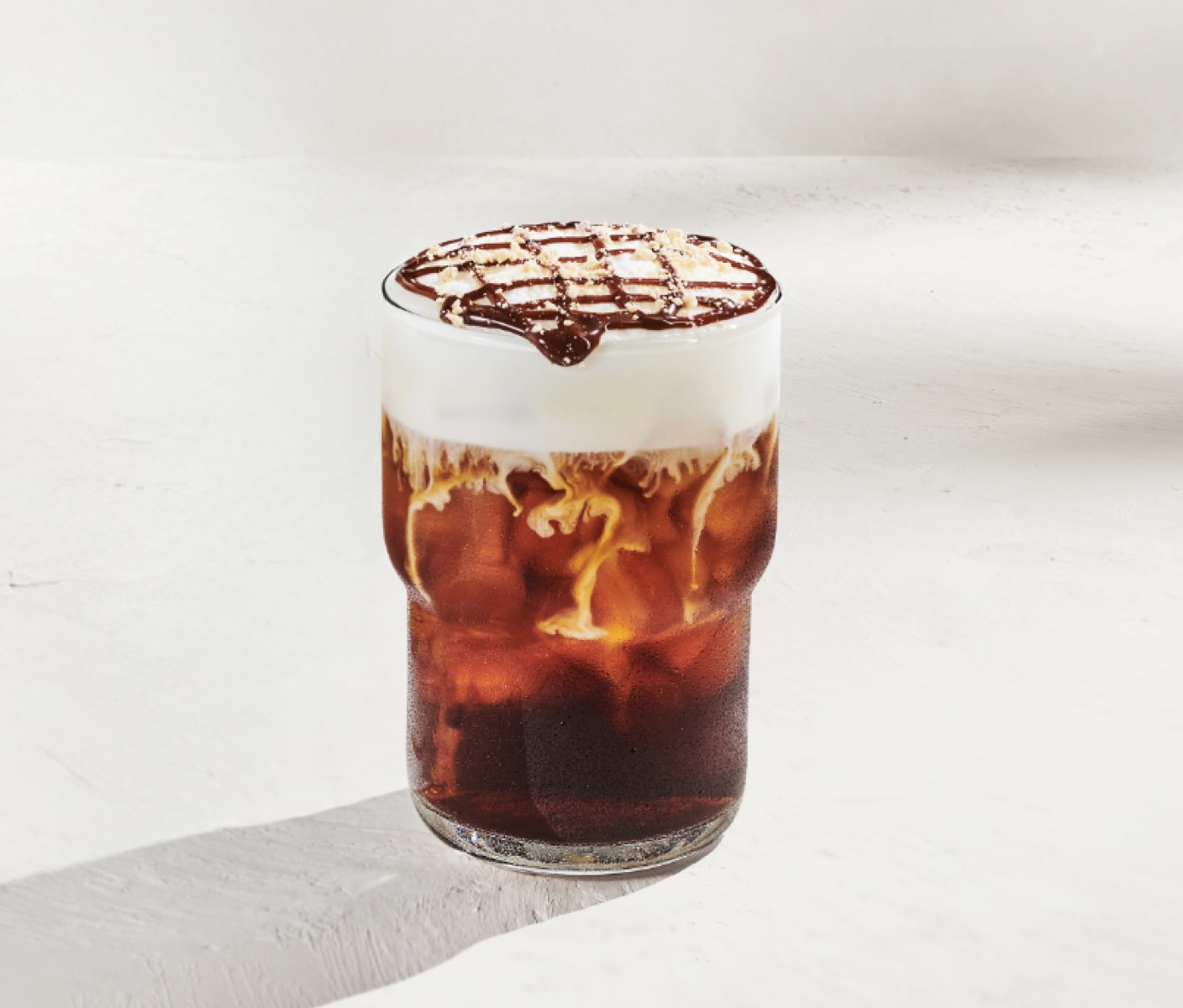A cold brew coffee in a glass topped with creamy cold foam and chocolate drizzle, topped with graham cracker crumble.