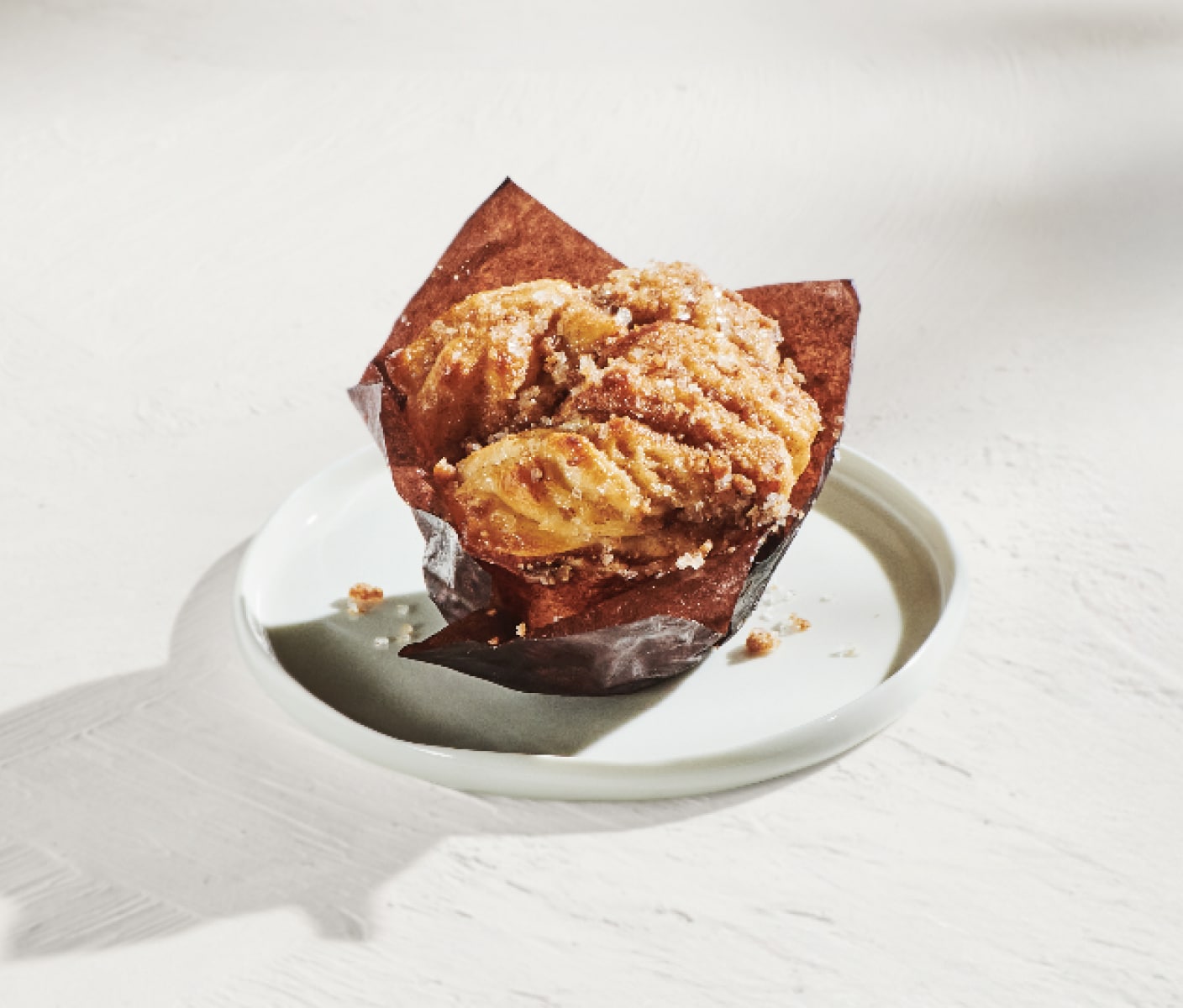 A pastry topped with cinnamon on a white serving plate wrapped in brown paper on a sunny white background.