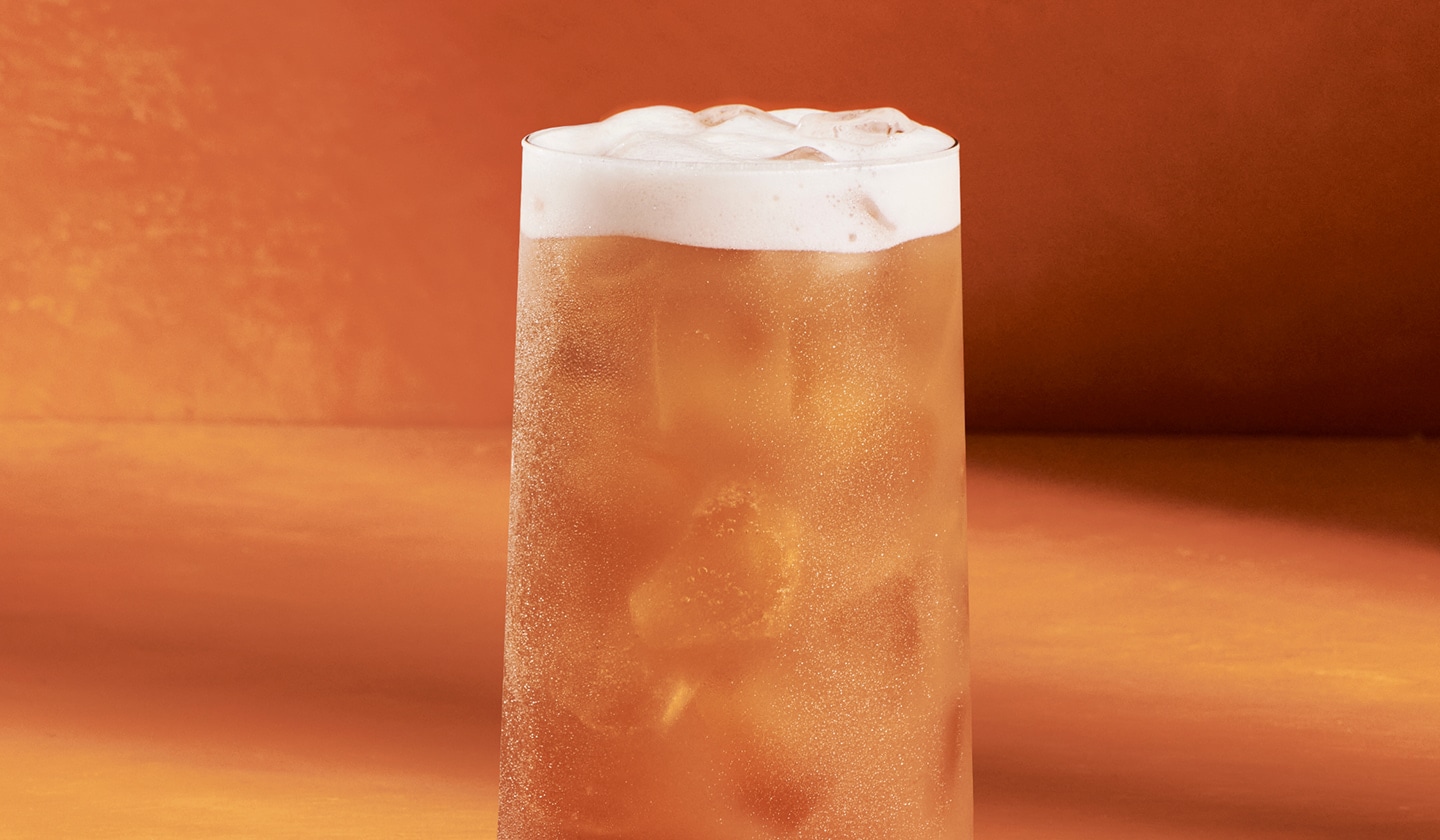 An iced orange drink with a layer of foam in a glass.