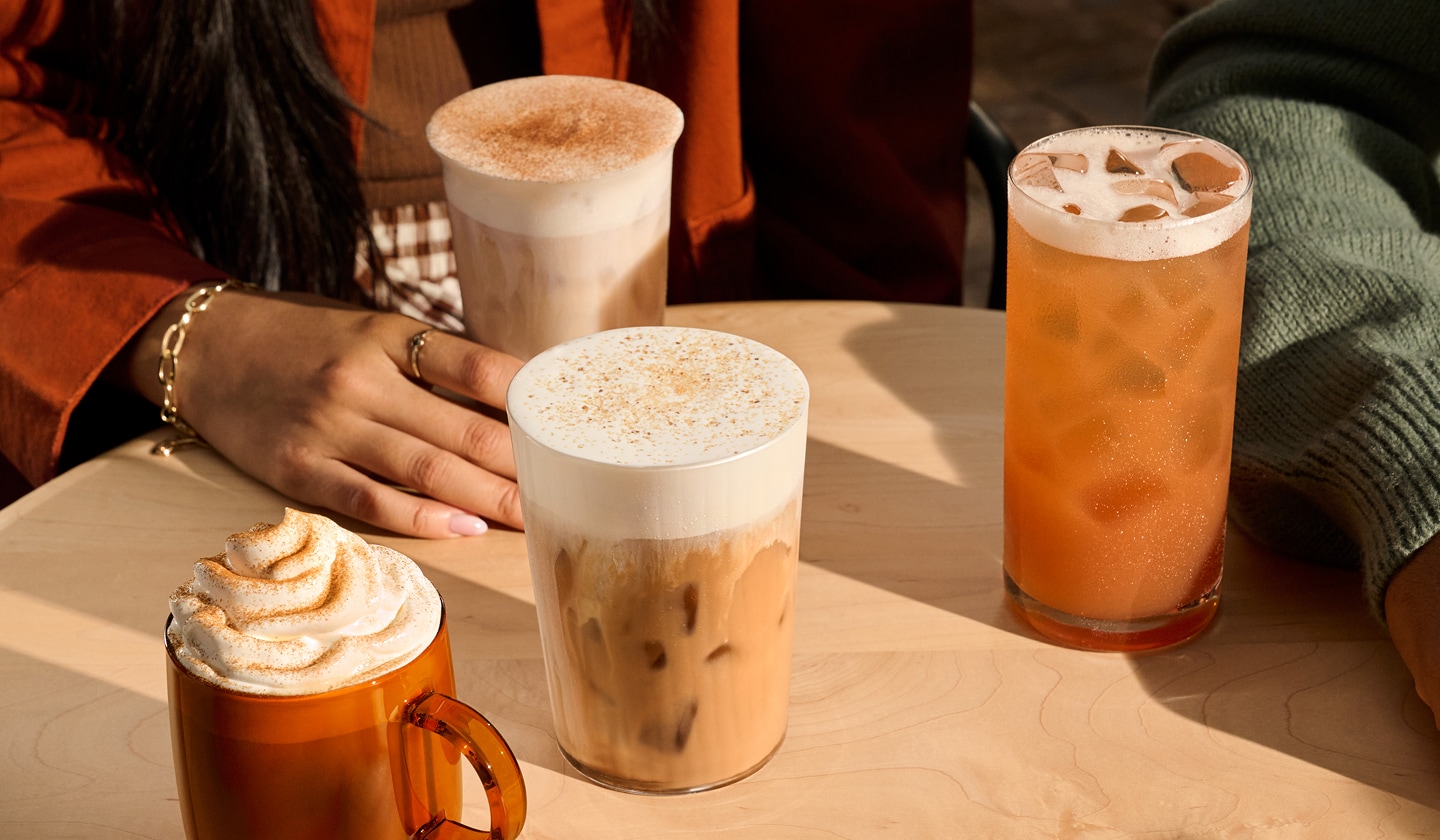 Four fall drinks on a table with hints of people gathered around them.