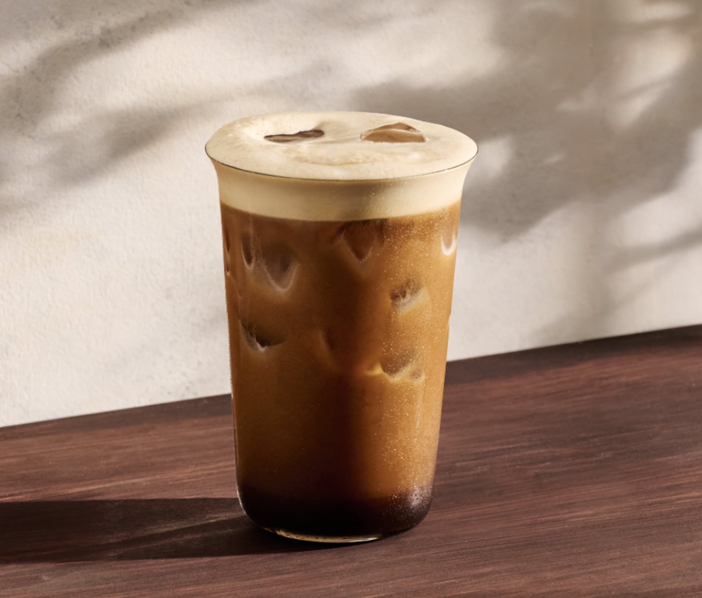 A Caramel Aerocano in a tall glass with ice. A light layer of foam rests at the top and deepens into bold espresso toward the bottom.