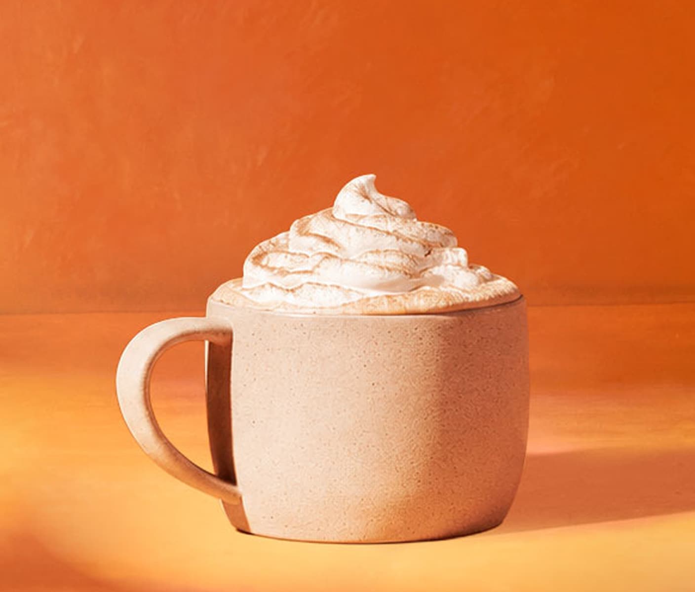 A hot drink topped with whipped cream and spices in a mug.