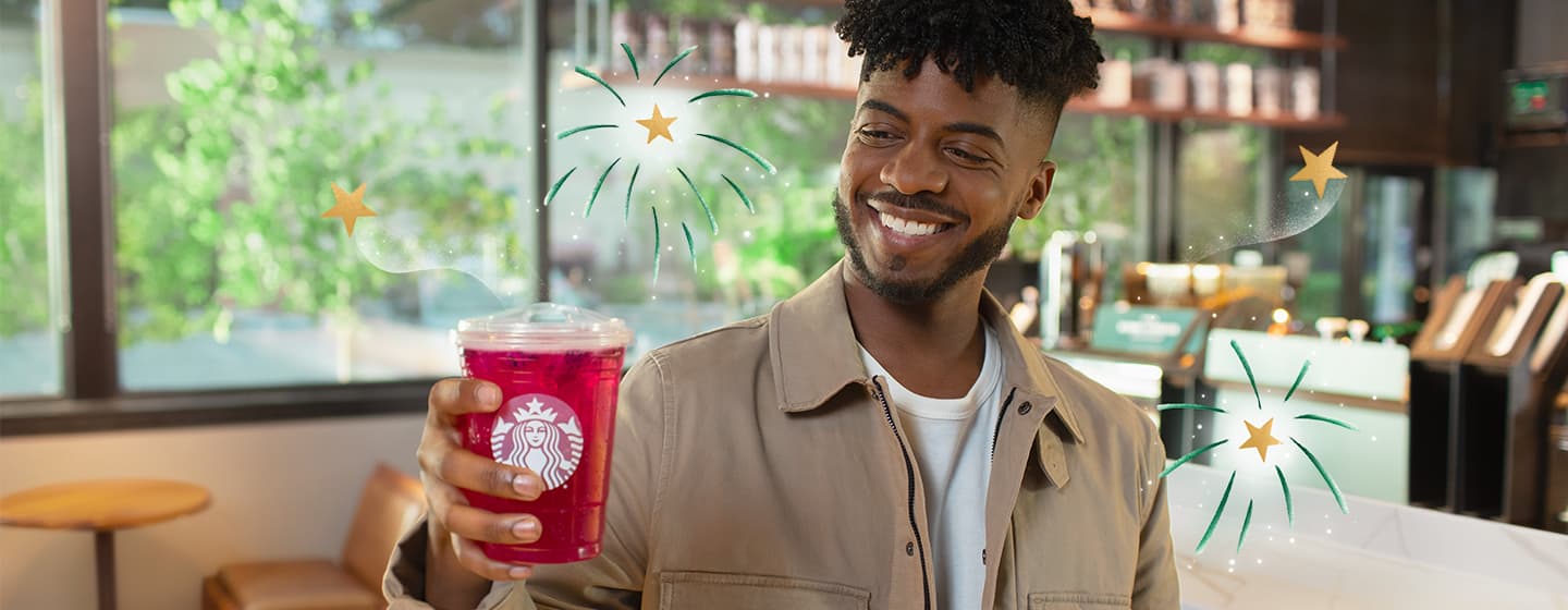 A man holding a Starbucks drink while fireworks burst around him.