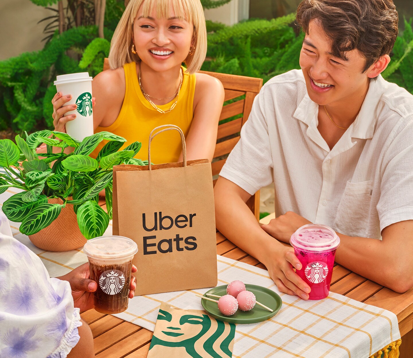 People gathered at a backyard table with Starbucks drinks, food and an Uber Eats delivery bag.